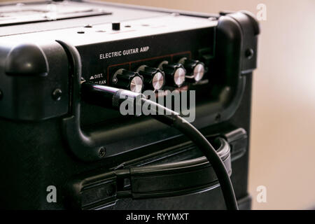 Gitarrenverstärker mit Rädern und Regler für Volume, Gain, Bass, Treble. Jack Kabel angeschlossen. Schwarz Amp mit rotem Licht auf. Stockfoto