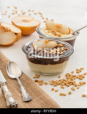 Schokolade und Vanille Pudding mit Pinienkernen und Asiatische birne Schichten in einer Glasschalen auf weißem Hintergrund. Gesunde, schmackhafte, glutenfreies Frühstück Stockfoto