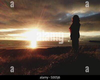 Frau stehend auf Sanddünen beobachten Sonnenuntergang Stockfoto