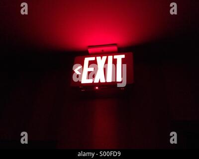 Eine leuchtende rote Notausgangsschild beleuchtet in völliger Dunkelheit. Ausfahrt auf der linken Seite. Stockfoto