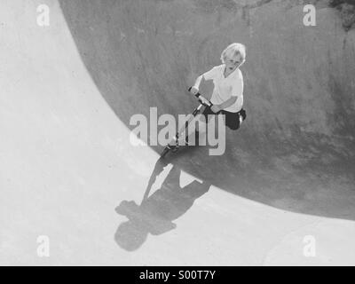 Kleiner Junge reitet auf seinem Roller zu einem Skatepark. Stockfoto