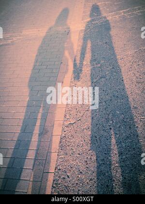 Lange Schatten von ein paar Hand in Hand mit einer rosa Besetzung Stockfoto