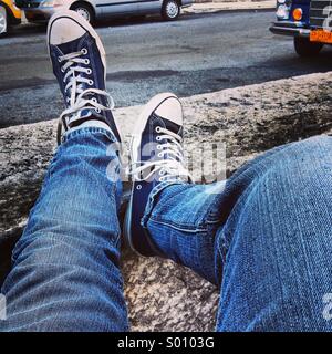 Ein Beinpaar Mannes gekleidet in Jeans und alte Turnschuhe lehnen Sie sich zurück auf einen Steinblock Stockfoto