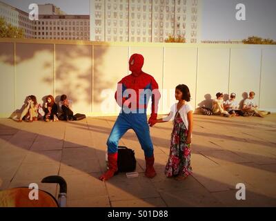 Ein Mann gekleidet wie Spider-Man in der Sonne auf der Südseite des Kindes Hand hält in London Bank Stockfoto