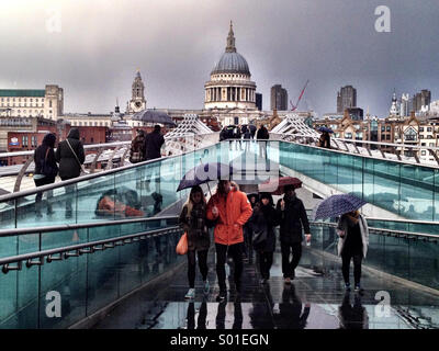 Menschen, die Sonnenschirme überqueren der Millennium Bridge in London an einem feuchten Frühlingstag Stockfoto