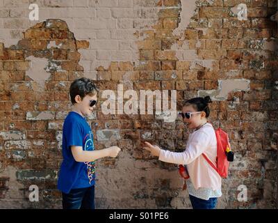 Zwei Kinder, ein Junge und ein Mädchen spielen Rock Paper Scissors vor einer Mauer. Farbe. Stockfoto