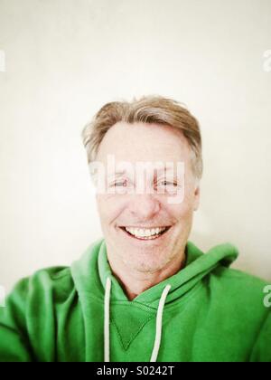 Glücklich lächelnd reifen Mann in seinen Vierzigern, trägt einen grünen Kapuzen Top. Stockfoto