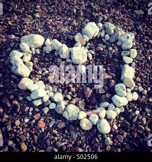 Ein Herz mit weißen Steinen und Kieseln an einem bunten Strand gemacht Stockfoto