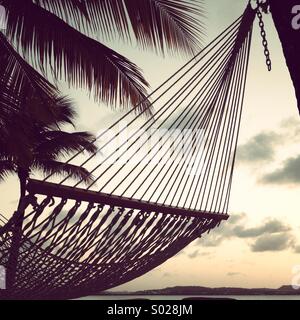 Hängematte am Strand bei Sonnenuntergang mit Palmen. Stockfoto