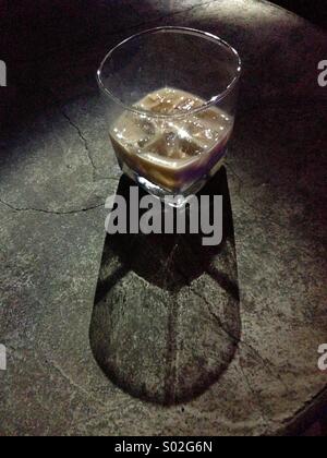 Glas von Baileys Likör auf Eis auf einem Steintisch mit Licht und Schatten. Alkoholisches Getränk. Stockfoto