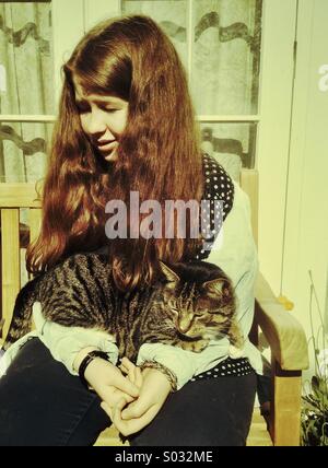 Mädchen mit Katze, Teenager im Alter von 14-16 Jahre im Freien mit Tabby Katze auf dem Schoß sitzen Stockfoto