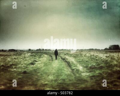 Einzelne Person Spaziergänge entlang einem grasbewachsenen Weg. Grunge-Effekt-Filter angewendet. Stockfoto