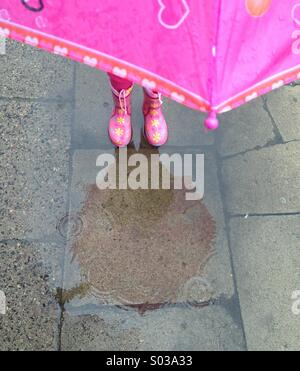 Kind in rosa Gummistiefeln in die Pfütze stehen Stockfoto