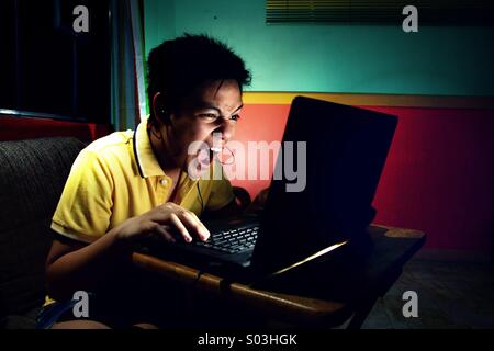 Asiatische Teen jungen spielen intensiv auf einem Laptopcomputer Stockfoto