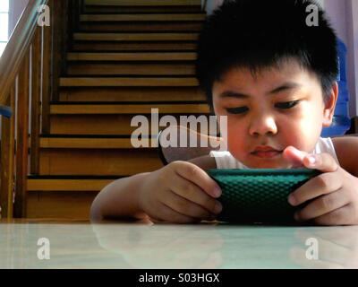 Junge asiatische Kind ansehen oder spielen auf einem Tablet Telefon Stockfoto