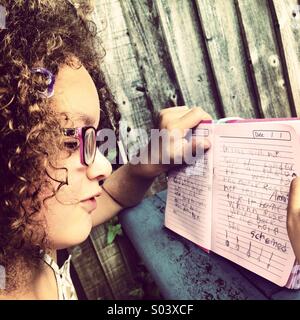 Lockige 6-jährigen Mädchenakt mit Brille lesen ihr Tagebuch. Stockfoto