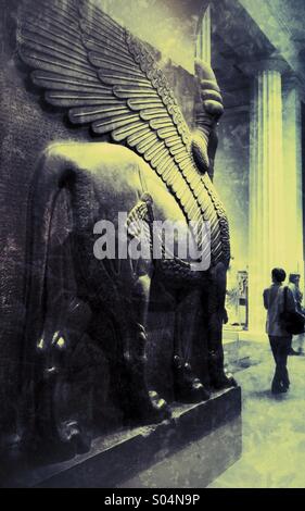 Eine Frau erforscht eine Galerie des British Museum in London, mit einer kolossalen Assyrian Statue eines geflügelten Löwen vom Palast Eingang des König Ashurnasirpal ihr überragt. Stockfoto