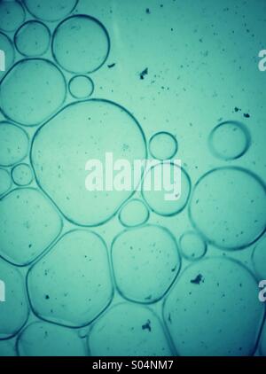 Flüssige Bläschen. Schließen Sie herauf Makro Bild Tropfen des Öls in blauer Farbe Wasser schweben. Stockfoto