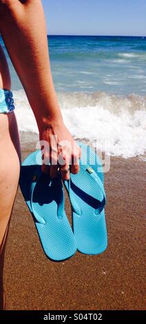 Frau am Strand mit blauen Flip Flops, Meer im Hintergrund Stockfoto