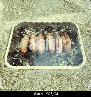 Ein halbes Dutzend Würstchen auf einem Einweg-Grill Stockfoto