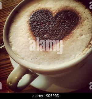 Cappuccino Kaffee trinken in große Tasse und einer herzförmigen Schokolade Form auf dem Schaum Stockfoto