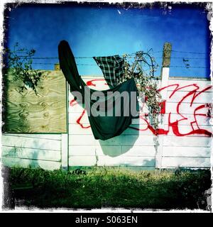 Betonschutzwand Wand mit Graffiti und alte Kleidung auf. Strahlend blauer Himmel. Stockfoto