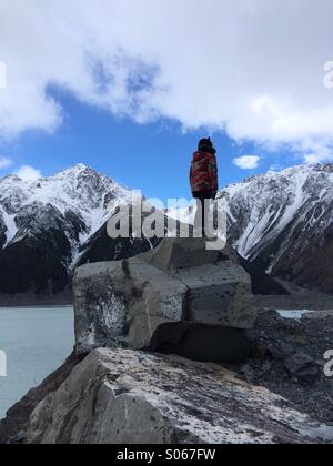 Der junge einen Bär Hut allein auf einer eiszeitlichen Findling Blick auf schneebedeckte Berge neben See Tasman Neuseeland Stockfoto