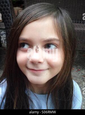 Ein junges Mädchen liebenswert lächelt mit einer kleinen Schnecke auf der Nase. Stockfoto