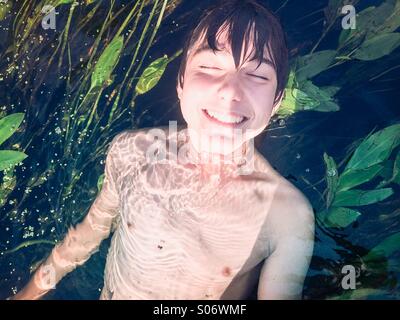 Lächelnde junge in einem reinen Fluss getaucht. mit üppigem Grün Stockfoto