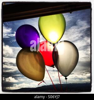 Bunten Ballons vor der Sonne vor einem Fenster vor blauem Himmel mit weißen flauschigen Wolken.