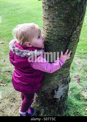 Es sind die einfachen Dinge: Babymädchen umarmt einen Baum, England. Einfache, aber leistungsfähige Unschuld. Stockfoto