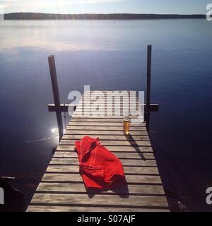 Ein kühles Bier und ein Handtuch auf einem Steg an einem idyllischen nordischen Sommerhaus See im Norden Finnlands Stockfoto