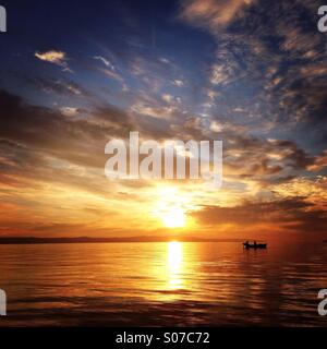 Sonnenuntergang auf dem Meer mit Sonnenstrahlen und kleines Boot Stockfoto