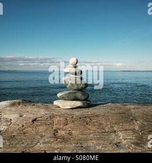 Steinhaufen gestapelt oder ausgewogene Steine auf Treibholz am Strand sitzen. Stockfoto