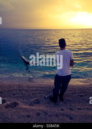 Fischer mit Fischernetz am Strand bei Sonnenuntergang Stockfoto