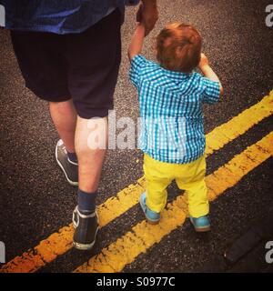 Vater und Sohn zu Fuß über doppelte gelbe Linien auf einer Straße in London. Stockfoto