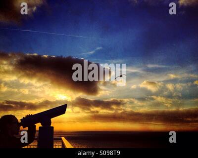 Junges Mädchen mit Teleskop Silhouette gegen Sonnenuntergang als Möwe fliegt vorbei Stockfoto