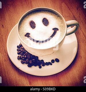 Kaffeepause - ein Cappuccino mit einem Schokoladenpulver Smiley und Kaffeebohnen auf der Untertasse Stockfoto