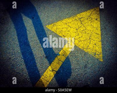 Gelbe Pfeilzeichen und Fußgänger Schatten auf asphalt Stockfoto