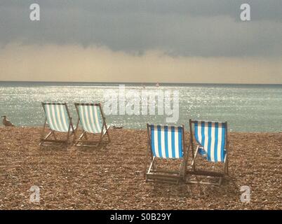 Vier gestreifte leere Strandkörbe mit Sonne auf zehn an einem Kiesstrand in Brighton, England. Stockfoto