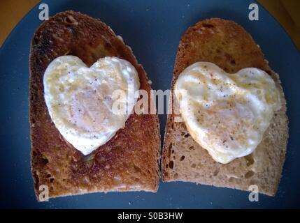 Herzförmige Spiegeleier auf Sauerteig-Toast. Valentinstag Frühstück. Stockfoto
