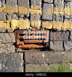 Gusseisen Gosse Gitter an der Seite einer Straße mit zwei gelben Linien gebrochen Stockfoto