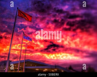 Ein roter Sonnenuntergang hinter den Fahnen vor dem Bahnhof Ebbsfleet Kent. Stockfoto