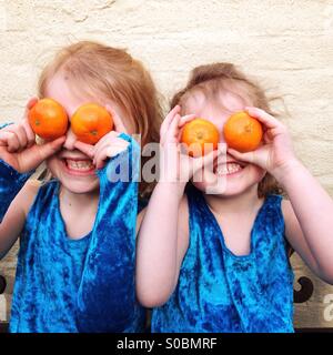 Kinder mit orangefarbenen Augen. Zwei Schwestern holding Orangen über ihre Augen, als ein Spiel, das illustrieren konnte einen hohen Gehalt an Obst in einer Diät zu essen. Stockfoto
