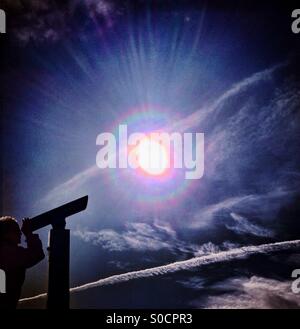 Mädchen mit Teleskop in der Silhouette gegen die helle Sonne bei bewölktem Himmel Stockfoto