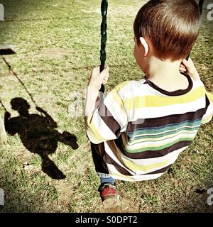 Kleiner Junge schwingt und bewundert sein Schattenbild Stockfoto