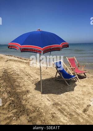 Erste Sonne am Strand, Blick auf einen Sonnenschirm und zwei Liegestühlen bei einem Frühlingstag Stockfoto