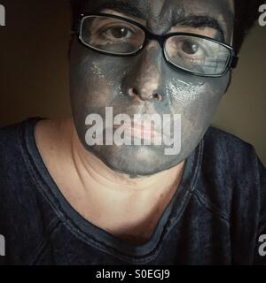 Eine Frau mit Brille mit einer Schlamm-Maske im Gesicht Stockfoto