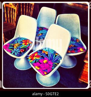 Vier Retro-weißen Kunststoff-Sockel-Stühle mit floralen Kissen Stockfoto