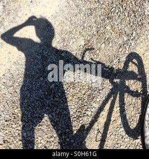 Schatten eines Mannes, der Wasser trinkt, der neben einem Mountainbike in der Toskana steht. Stockfoto